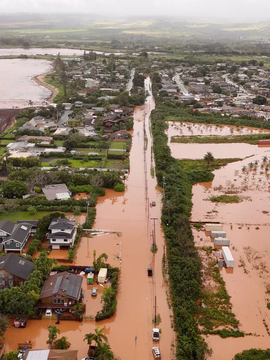 An aerial view of a flooded neighbourhood, brown water covering the road and fields between the houses.